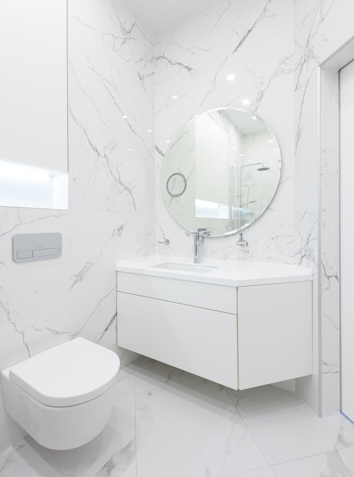 A sleek, minimal bathroom with white marble walls and round mirror.